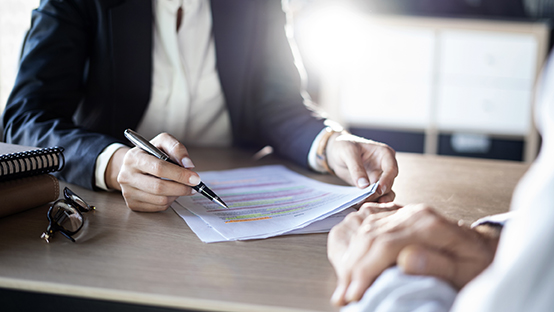 person writing on a piece of paper at table with another person