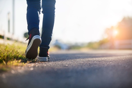 Low-perspective shot of person's legs and feet walking down an empty road