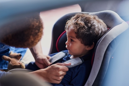father strapping son into car seat