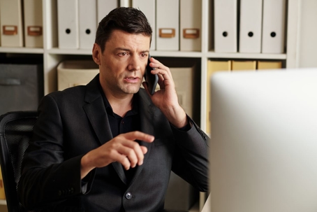 Man on the phone pointing at his computer