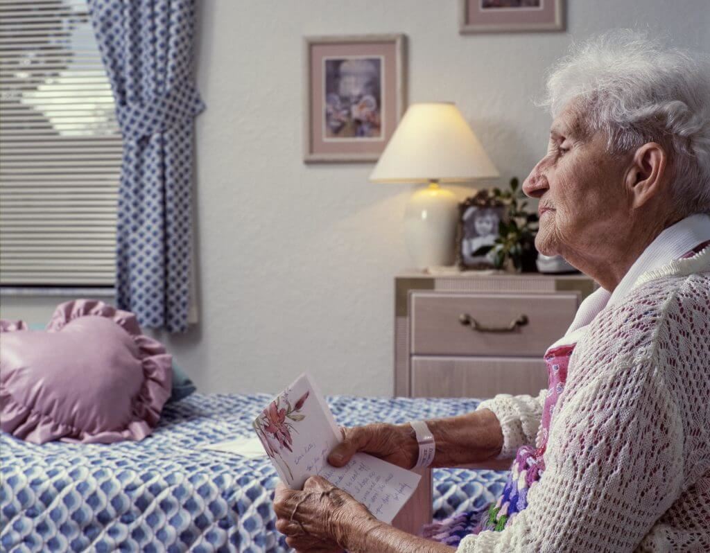 elderly woman reading a letter and staring sadly out the window